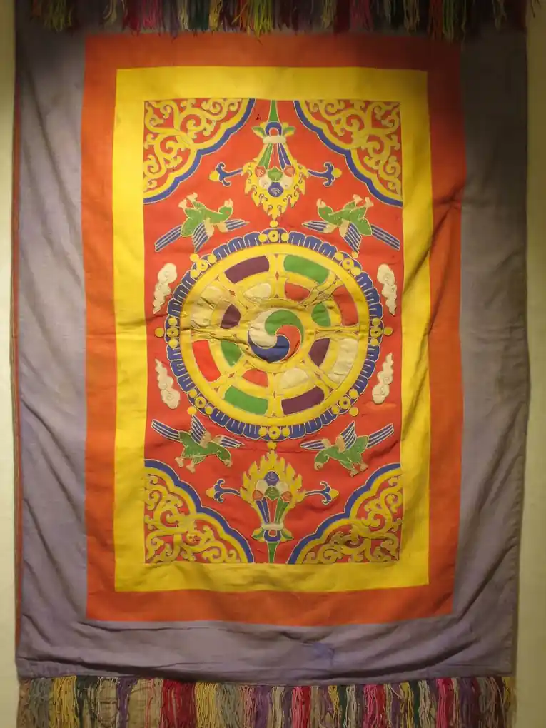 A hanging appliqué cover with a round medallion in red, yellow and green, framed by layered borders