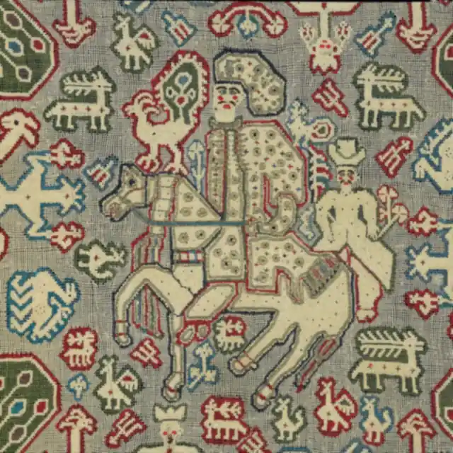 Close view of dense embroidery: a horse and rider among small birds and octagon motifs in red, green and ivory thread